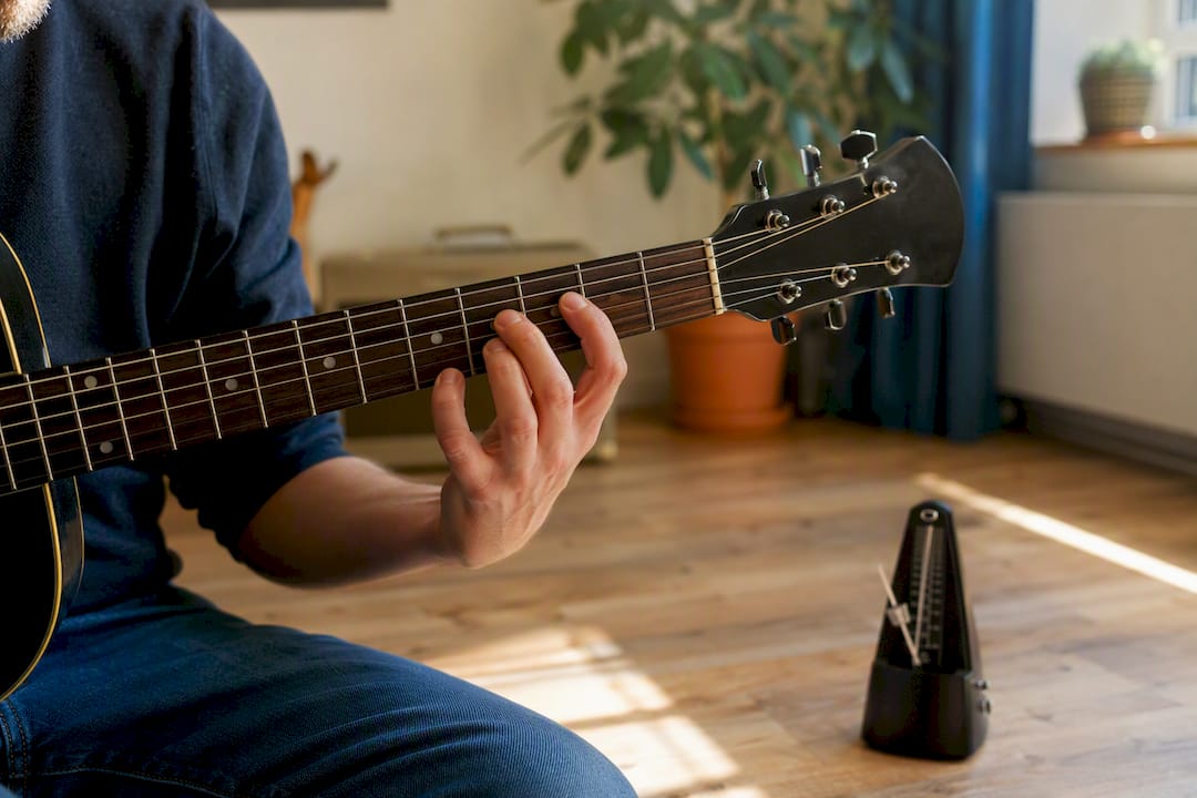Hand op een snaar van de gitaar die intervallen oefent bij een metronoom